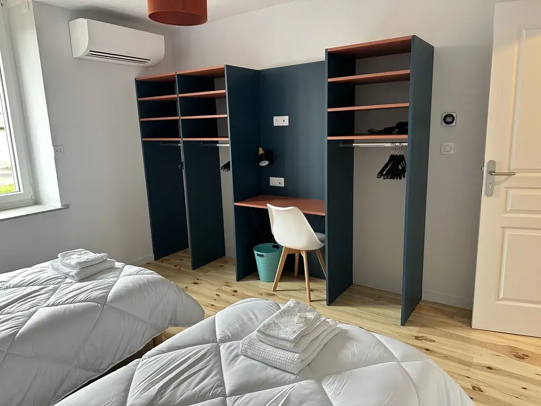 Chambre gîte La Bamboche Chambre moderne du gîte La Bamboche à Lapte, avec trois lits simples, espace bureau et rangements ouverts.