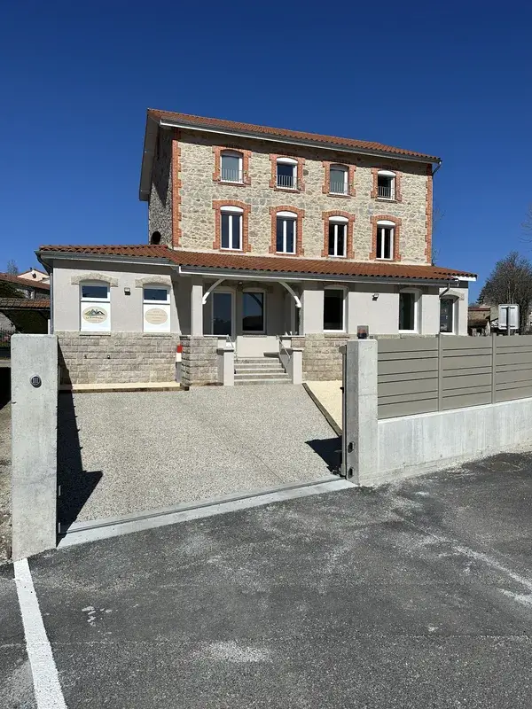 Vue frontale de la façade du gîte La Bamboche à Lapte avec entrée principale, portail ouvert et ciel bleu.