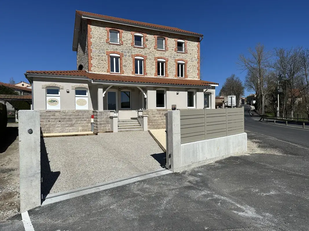 Façade du gîte La Bamboche à Lapte, bâtiment en pierre rénové avec parking et portail d’entrée.
